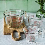 Miarki kuchenne ze szkła, na tle zielonej ściany, idealne do pomiaru składników w domowym gotowaniu i pieczeniu.