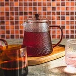 Słój z herbatą na drewnianym podkładce z kolorowym tłem, idealny do relaksu i cieszenia się chwilą, domowy sposób na aromatyczne napoje i sprzyjającą atmosferę w domu.