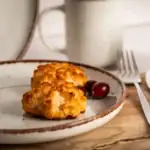 Pikantne kotleciki kokosowe na białym talerzu, obok czerwone winogrona, z szklanym dzbankiem i widelcem na drewnianym stole, idealne na zdrowe i smaczne danie, domowe przepisy, kuchnia polska, zdrowe posiłki.