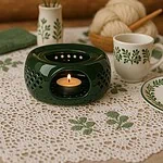 Ciepła dekoracyjna lampka z świecą w ceramicznym naczyniu, zestaw z filiżankami i serwetką na rustykalnym stole z kwiatami, idealny do domowego zakątka relaksu i odpoczynku.