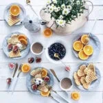 Orazędzi z oranżadą i owocami, na białym tle, wspólny brunch z domowymi goframi, świeżymi jagodami, figami i kwiatami na decorative wooden tray, w stylu skandynawskim, idealny na śniadanie lub spotkanie przy kawie.