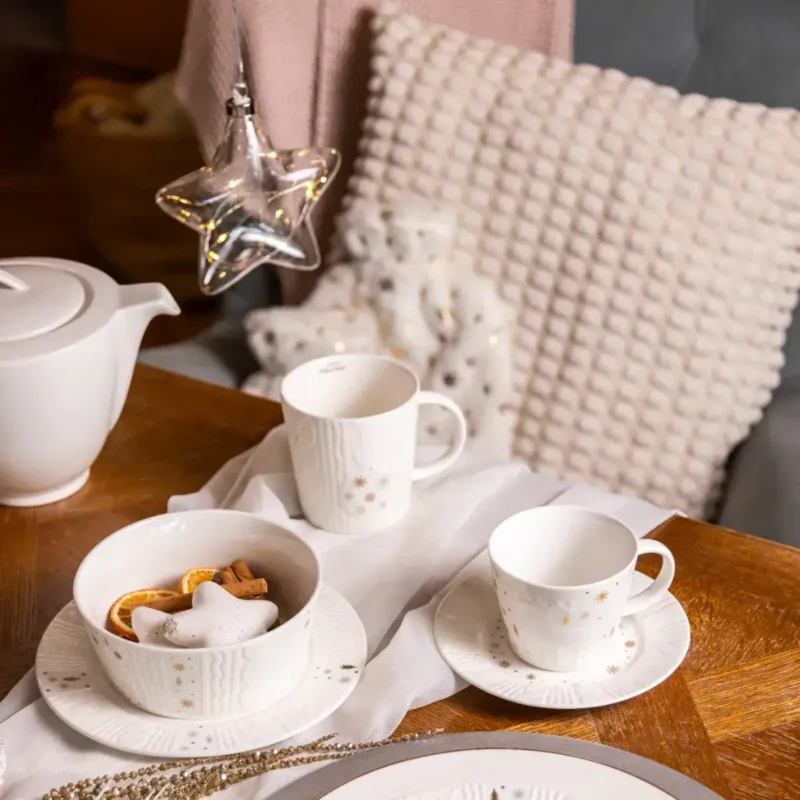 Ładne porcelanowe naczynia do kawy i herbaty w świątecznym stylu na drewnianym stole z ozdobami świątecznymi i ciepłymi światłami, idealne na zimowe wieczory i święta bożonarodzeniowe.