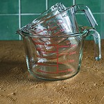 Szklane miarki do pomiaru płynów, zlewki i miarki kuchenne, przechowywanie i odmierzenie składników, nowoczesny design, z zielonym tłem z płytek ceramicznych, praktyczne akcesoria kuchenne, Domowy Zakątek, wysokiej jakości akcesoria kuchenne, wygoda i precyzja w pomiarze, funkcjonalne naczynia do kuchni.