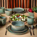 Talerze i filiżanki z porcelany w turkusowym odcieniu z złotymi detalami na drewnianym stole, idealne do domowego użytku i aranżacji wnętrz w stylu rustykalnym, dodające ciepła i elegancji.