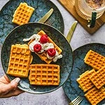 Delikatne gofry z bitą śmietaną i malinami na ceramicznym talerzu, idealne na śniadanie lub deser, domowy klimat, smaczne i chrupiące.