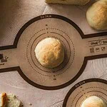 Miękkie ciasto na bazie naturalnych składników, gotowe do pieczenia, na stole kuchennym z funkcjonalną matą do wyrabiania i formowania wypieków, idealne do pieczenia chleba i bułek.