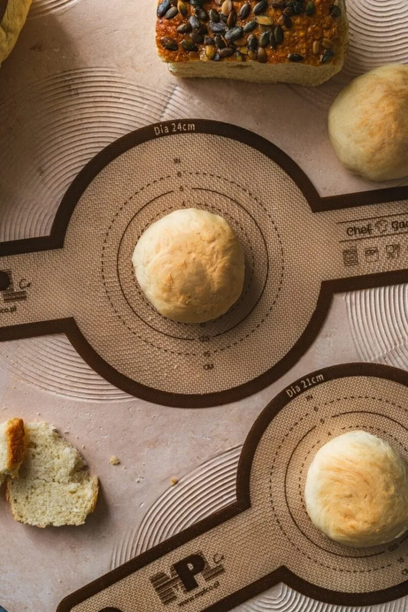 Miękkie ciasto na bazie naturalnych składników, gotowe do pieczenia, na stole kuchennym z funkcjonalną matą do wyrabiania i formowania wypieków, idealne do pieczenia chleba i bułek.