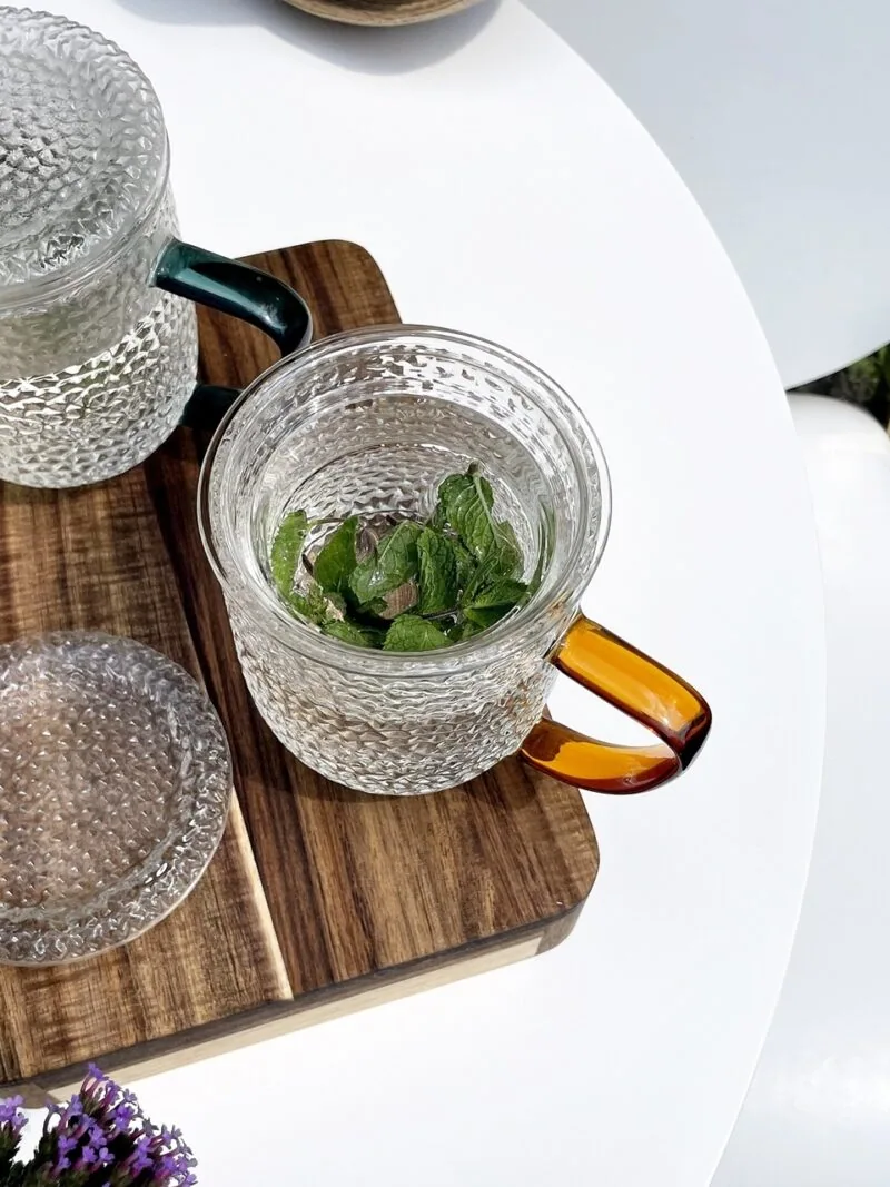 Schwarzebloggermętna herbata miętowa w szklance na drewnianej podstawce, z liśćmi mięty, elegancke i naturalne zestawienie do relaksu i zdrowego stylu życia.