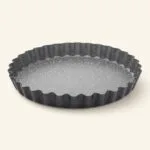 Czarna forma do tarty z falistymi krawędziami, idealna do pieczenia i serwowania wypieków, wykonana z wysokiej jakości materiałów ceramicznych i metalowych.