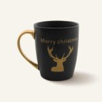 Miedziany uchwyt i złoty napis "Merry Christmas" na czarnym kubku ceramicznym z rysunkiem renifera, idealny na świąteczne okazje, element dekoracji kuchni i prezent świąteczny.