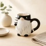 Przedmiotowy kubek z motywem zwierzęcia, czarno-biały, ceramiczny, na kawę lub herbatę, na stole z talerzem, miseczką i serwetką, idealny do kuchni, sklep domowyzakatek.pl.