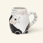 Ceramiczny kubek z czarnym i białym wzorem, ozdobiony gwiazdkami i różowymi elementami, idealny do kawy lub herbaty, na stronie domowyzakatek.pl, sklep z ceramiką i akcesoriami kuchennymi.