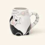 Ceramiczny kubek z czarnym i białym wzorem, ozdobiony gwiazdkami i różowymi elementami, idealny do kawy lub herbaty, na stronie domowyzakatek.pl, sklep z ceramiką i akcesoriami kuchennymi.