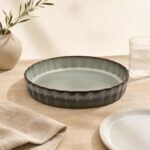 Patera ceramiczna w stylu rustykalnym na drewnianym stole, obok szklanka i talerz, dekoracja wnętrza kuchni, eleganckie naczynia do serwowania potraw, naturalne materiały, minimalistyczny design.