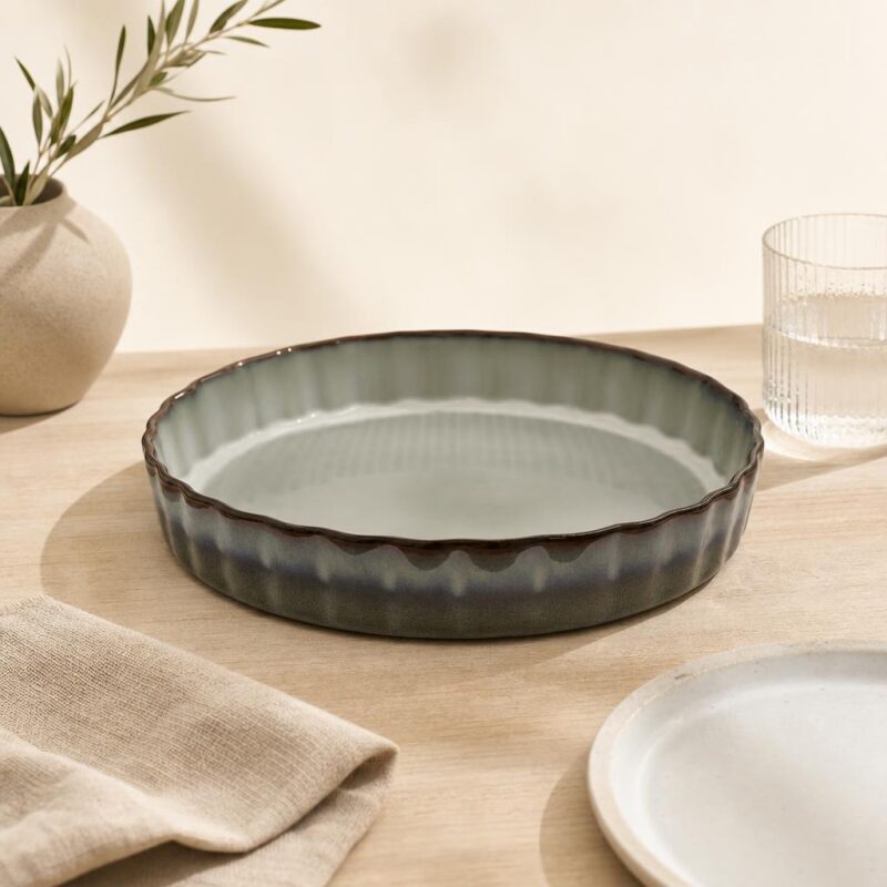 Patera ceramiczna w stylu rustykalnym na drewnianym stole, obok szklanka i talerz, dekoracja wnętrza kuchni, eleganckie naczynia do serwowania potraw, naturalne materiały, minimalistyczny design.