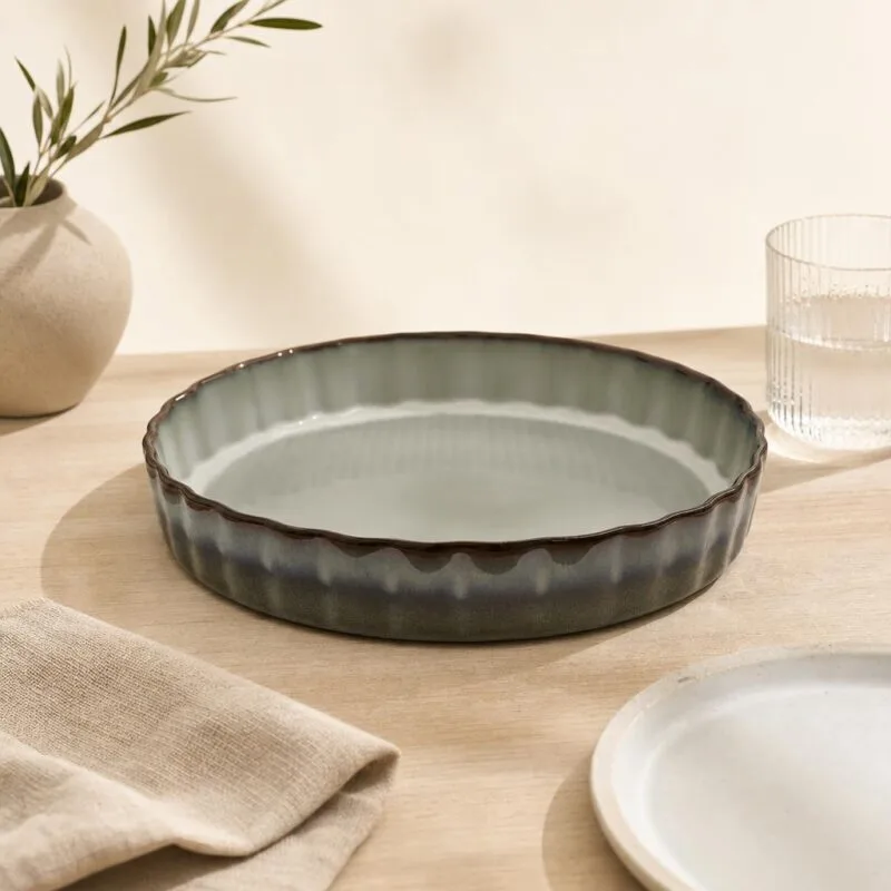 Patera ceramiczna w stylu rustykalnym na drewnianym stole, obok szklanka i talerz, dekoracja wnętrza kuchni, eleganckie naczynia do serwowania potraw, naturalne materiały, minimalistyczny design.