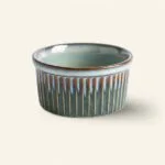Ceramiczna miska w odcieniach zieleni i brązu z pionowymi żłobieniami, idealna do serwowania potraw, element dekoracyjny kuchni lub jadalni.